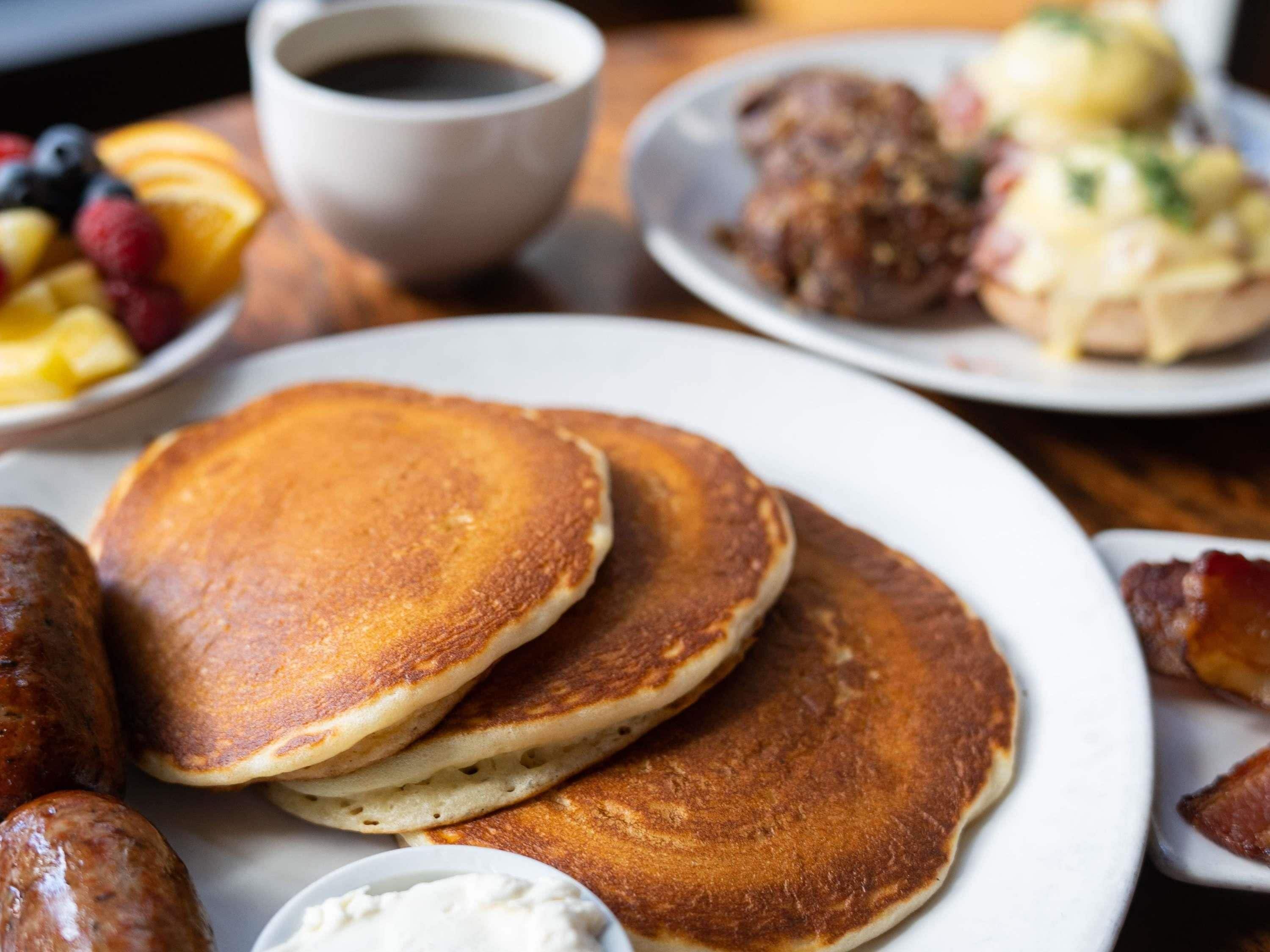 A breakfast setting with pancakes, sausages, and a cup of coffee.
