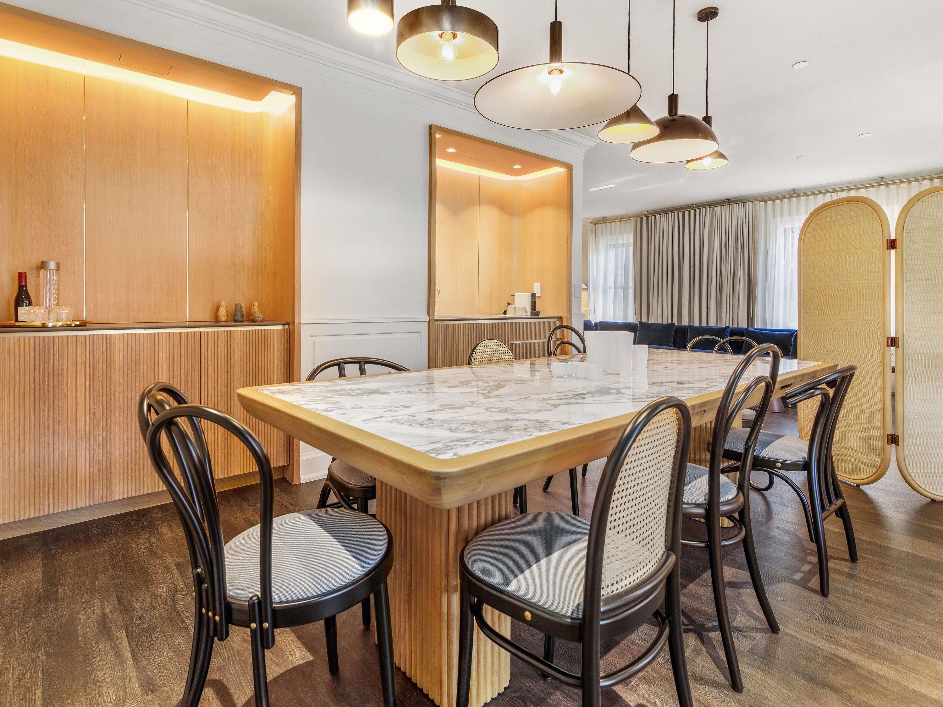 A modern dining area with a marble table, black chairs, wooden paneling, and pendant lighting.