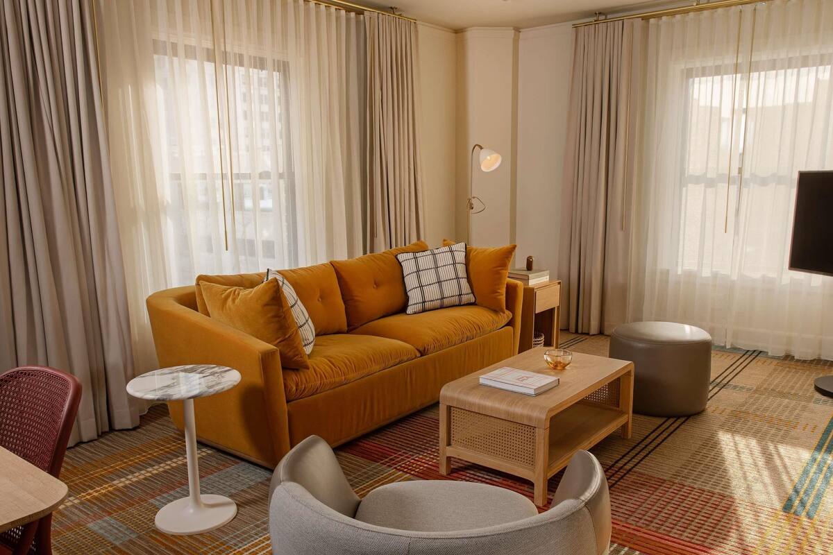 A living room with a mustard-colored sofa, a small round table, a chair, and a television.
