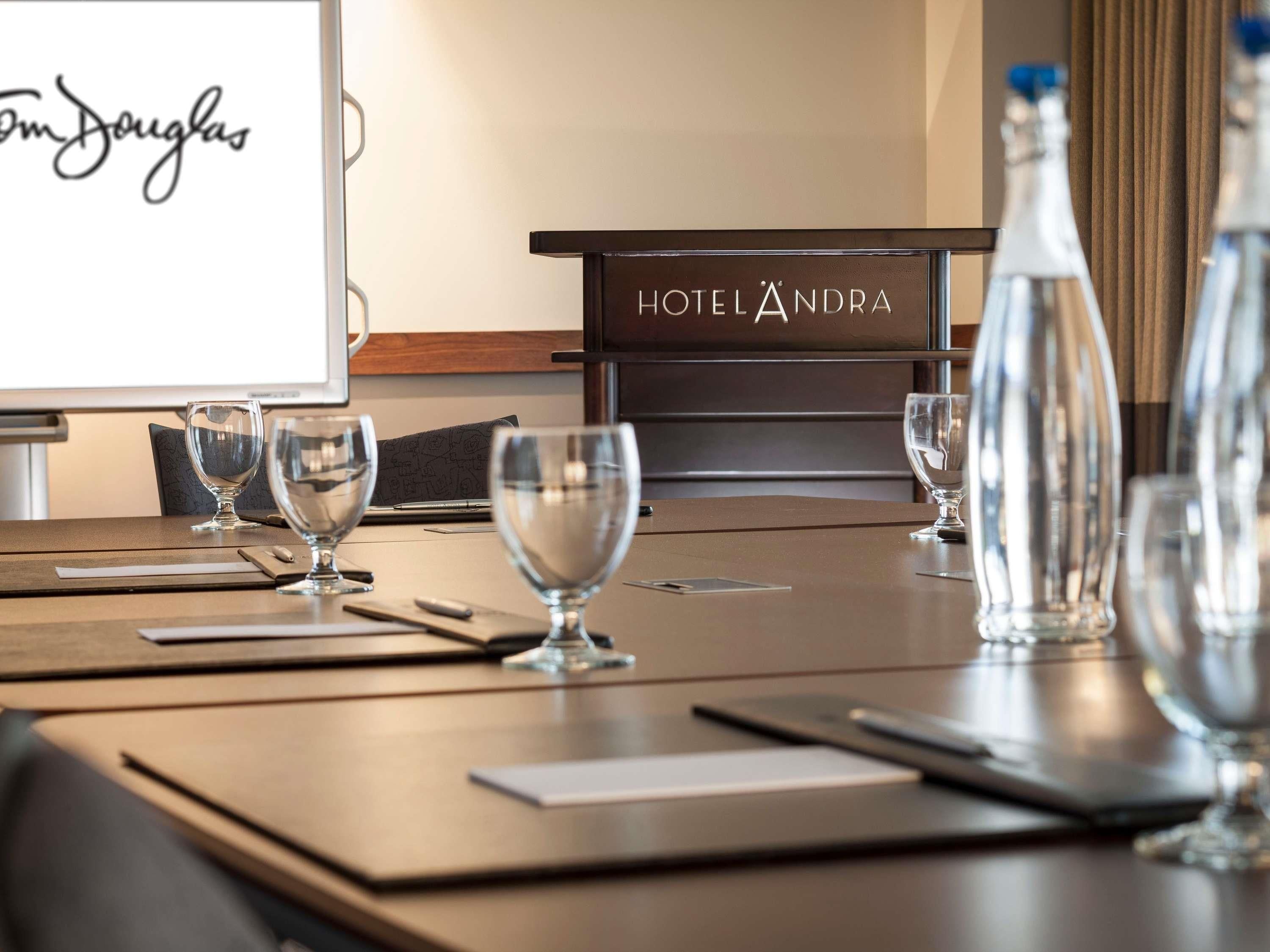 A hotel room with a conference table, empty wine glasses, a water bottle, and a sign reading 'HOTEL ANDRA'.
