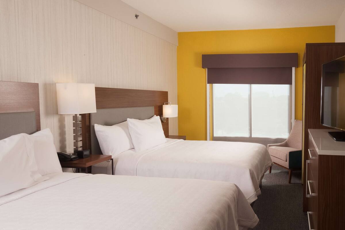 A hotel room with two beds, a desk, a chair, and a TV.