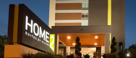 Un moderno edificio de hotel con un letrero llamativo que dice 'HOME 2 SUITES BY HILTON'.