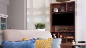 A modern living room with a brown sofa, a glass coffee table, and a TV on a wooden stand. - Home2 Suites by Hilton Atlanta Perimeter Center (Atlanta)