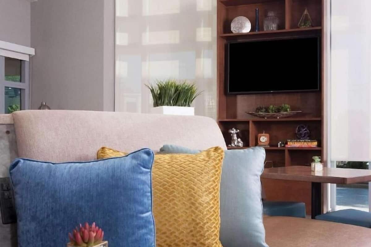 A modern living room with a sofa, a glass coffee table, a flat-screen TV, and geometric pendant lights.
