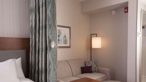 A hotel room with a bed, a sofa, a small table, a lamp, and a framed picture on the wall. - Home2 Suites by Hilton Atlanta Perimeter Center (Atlanta)