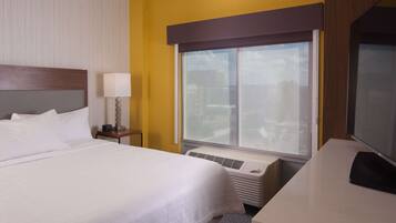 Habitación de hotel con cama, mesita de noche con lámpara, ventana con vistas y escritorio con silla.