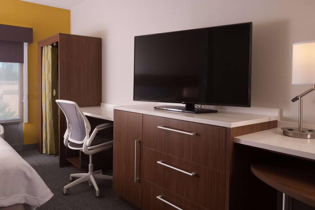 A hotel room with a bed, a desk with a computer, a TV, and a lamp.