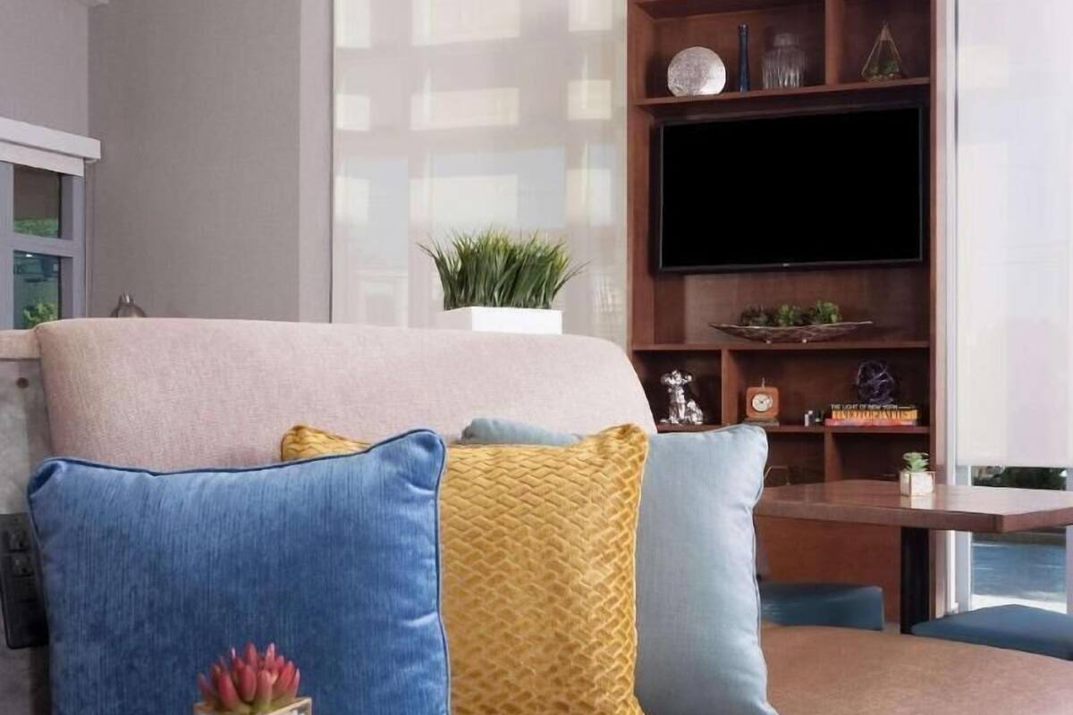 A modern living room with a sofa, a glass coffee table, a flat-screen TV, and geometric pendant lights.