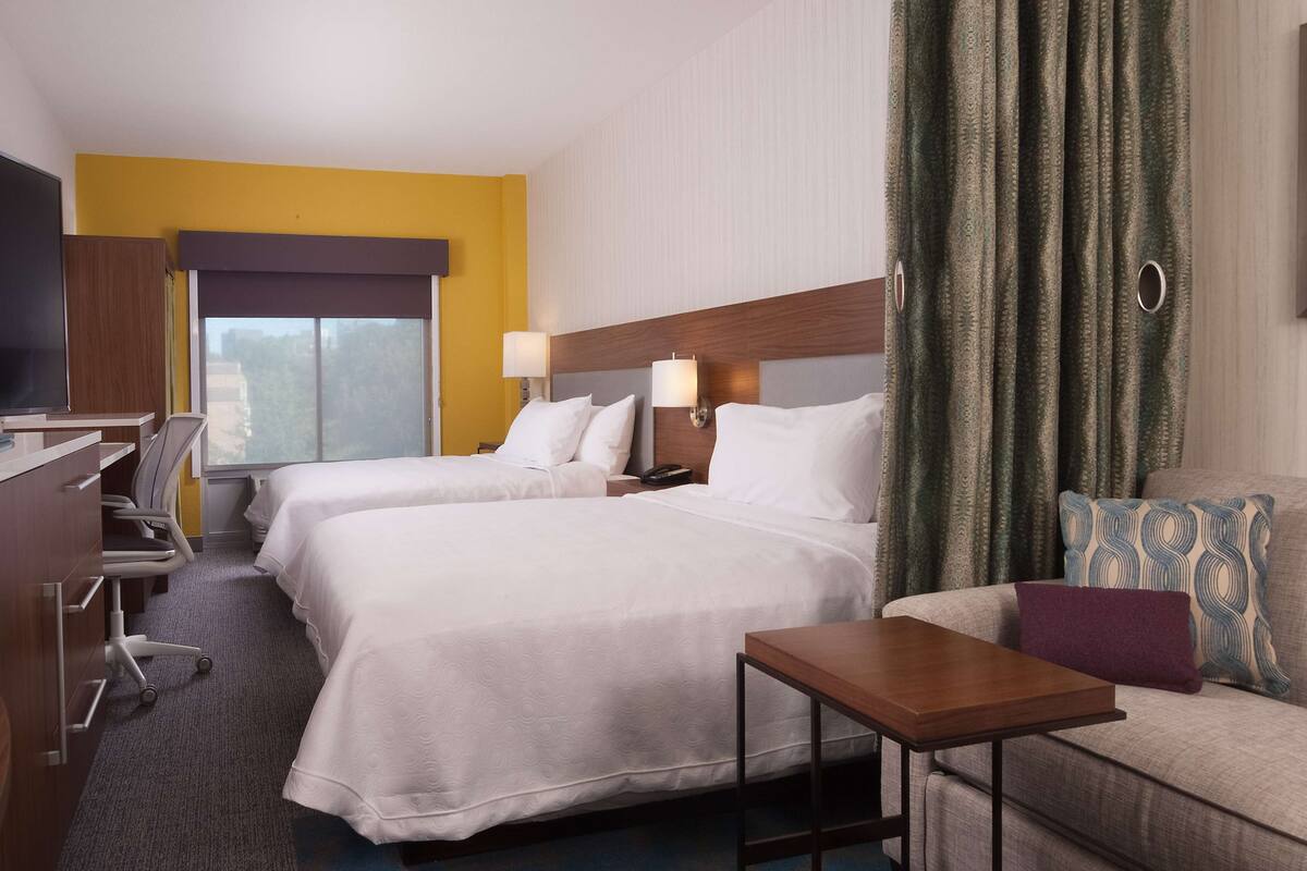 A hotel room with two beds, a desk, a chair, a small table, and a sofa.