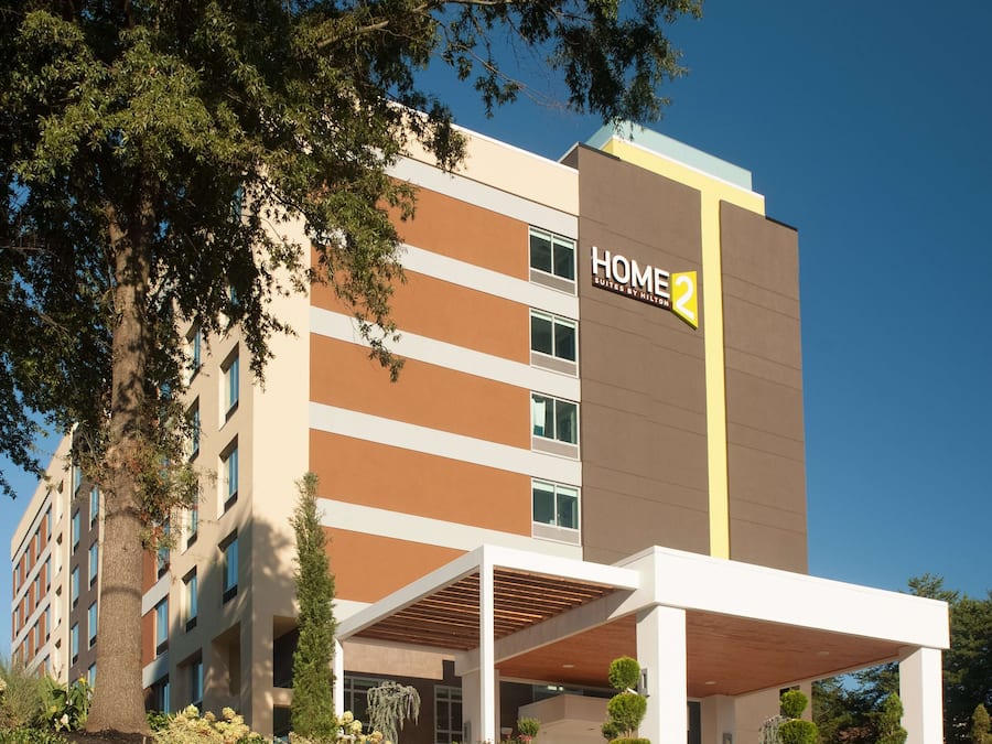 A modern hotel building with a sign reading "HOME 2 Suites by Hilton".