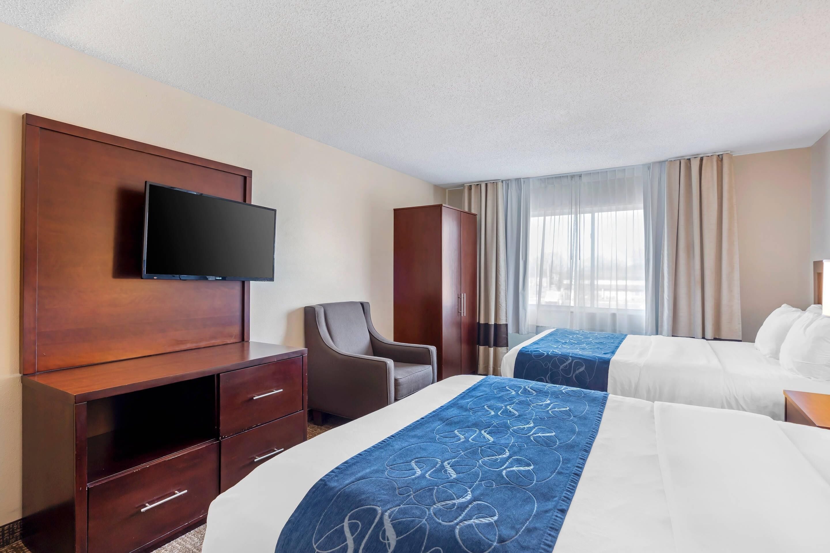 A hotel room with two beds, a TV, a desk, and a chair.