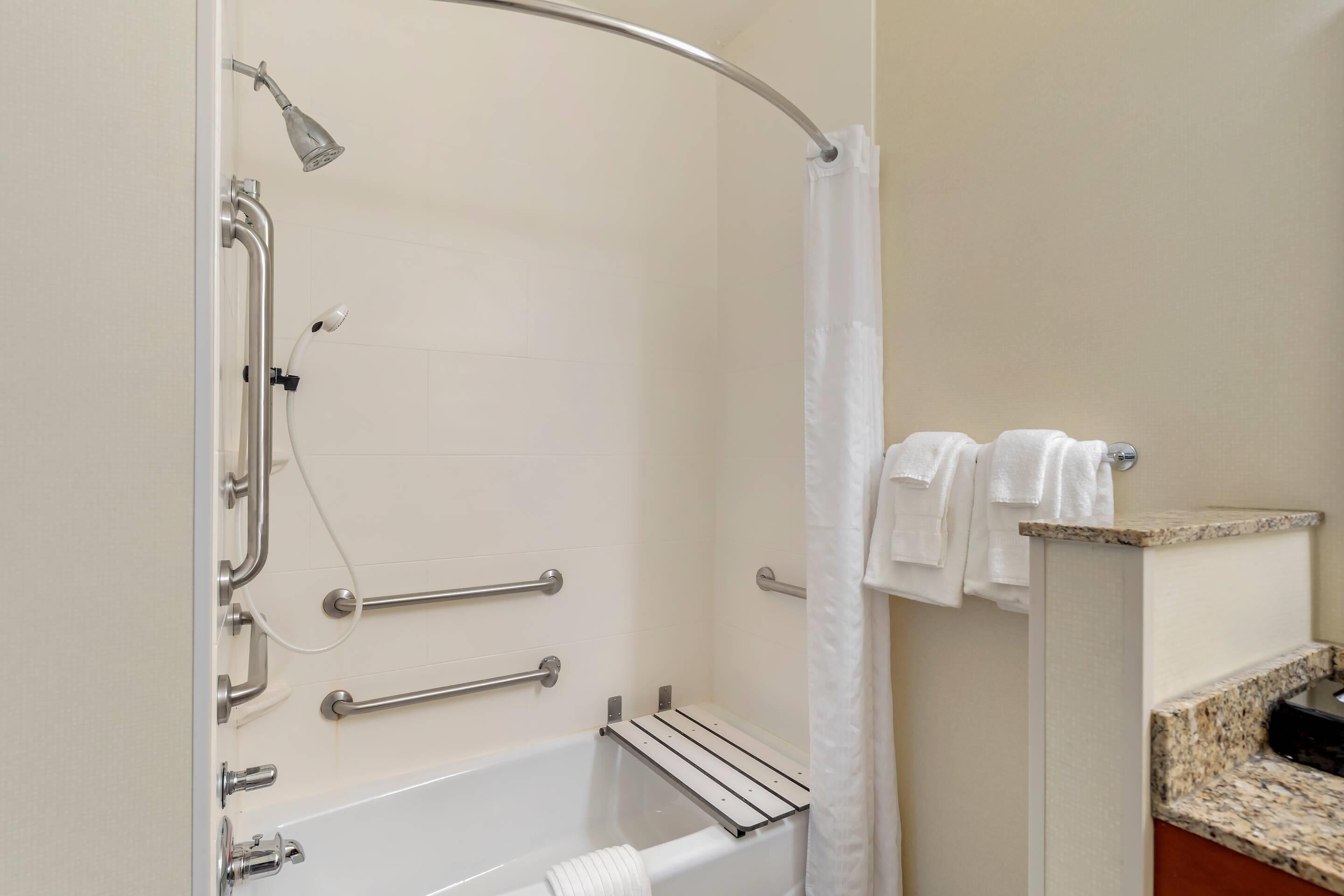 Une salle de bain équipée d’une baignoire, de barres d’appui, d’un pommeau de douche et d’un porte-serviettes.