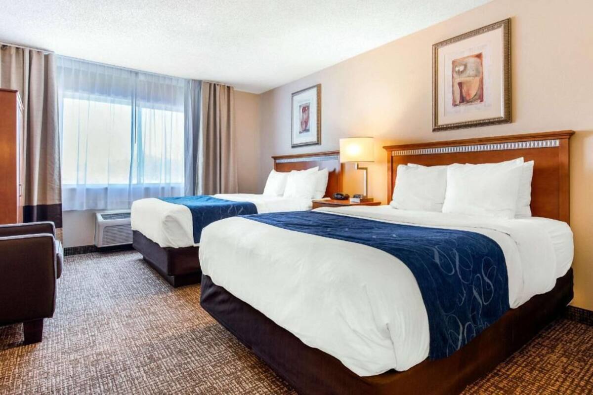 A hotel room with two beds, a desk, a chair, and a window with curtains.