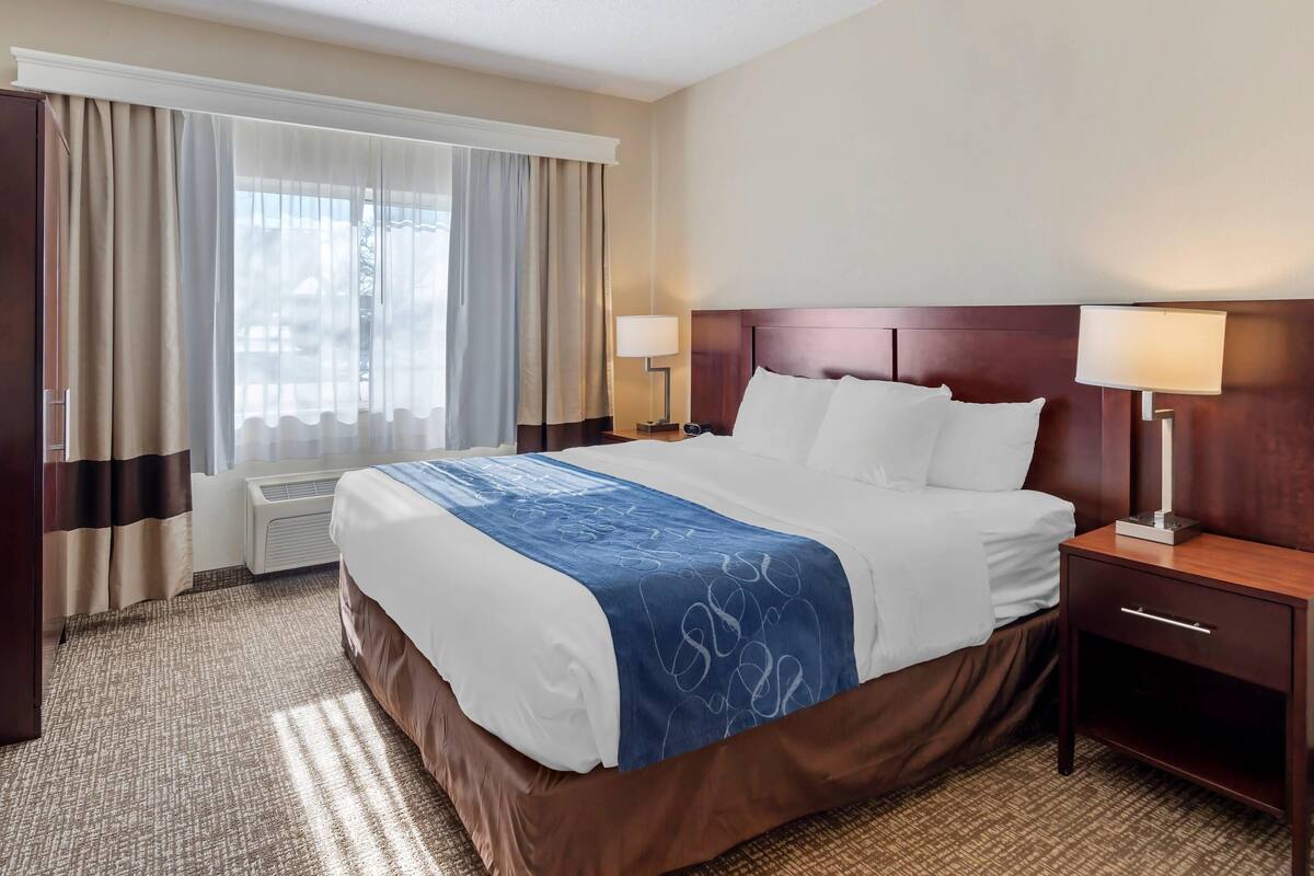 A hotel room with a large bed, two bedside lamps, a nightstand, and a window with curtains.