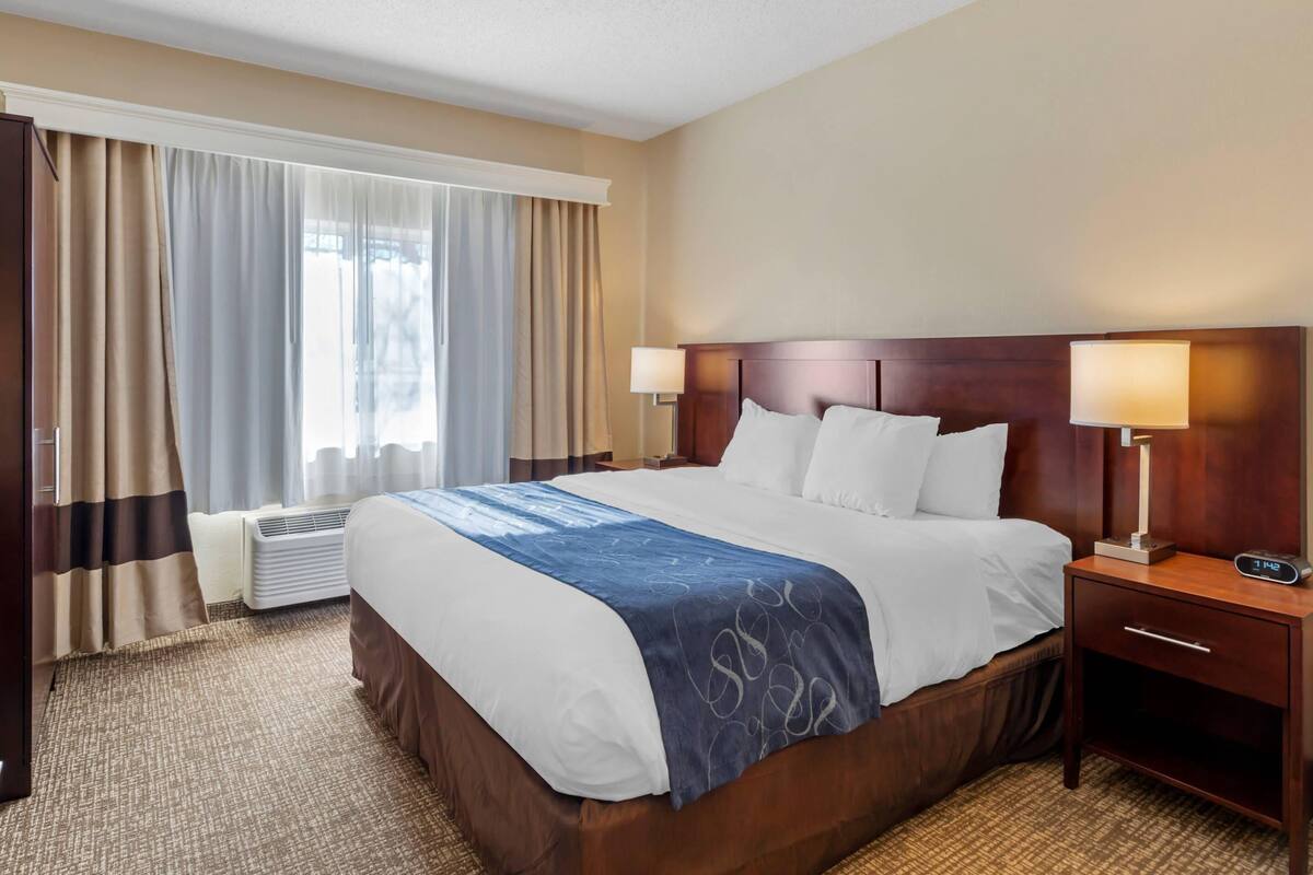 A hotel room with a large bed, two bedside lamps, a nightstand, and a window with curtains.