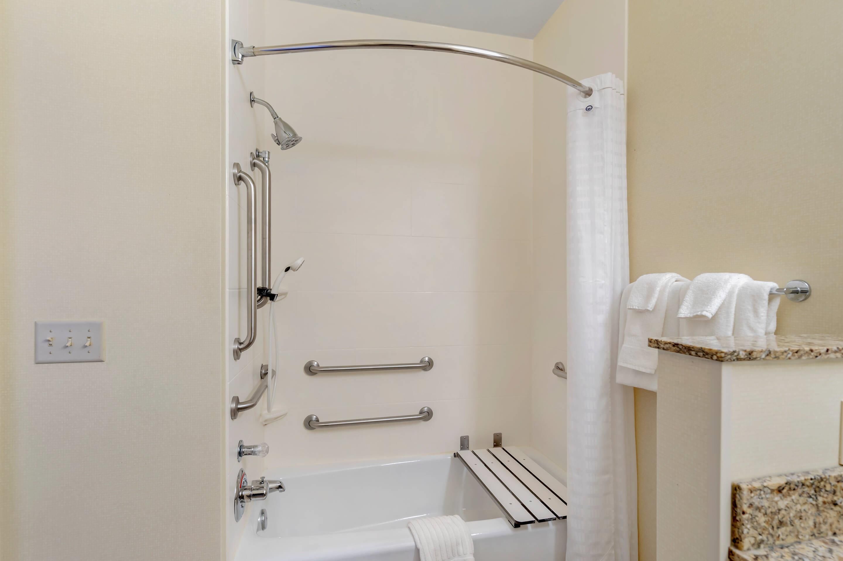 A shower with grab bars, a towel rack, and a bathtub.