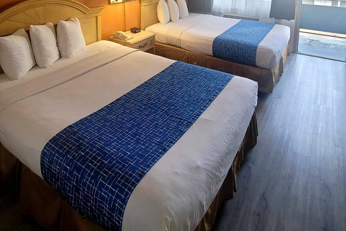 A hotel room with two beds, a nightstand with a lamp, a painting on the wall, and a window with curtains.