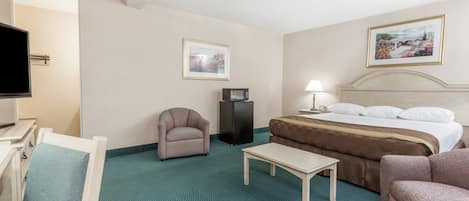 Quarto de hotel com uma cama, uma mesa de escritório, uma cadeira, uma mesinha, uma televisão e duas imagens emolduradas nas paredes.