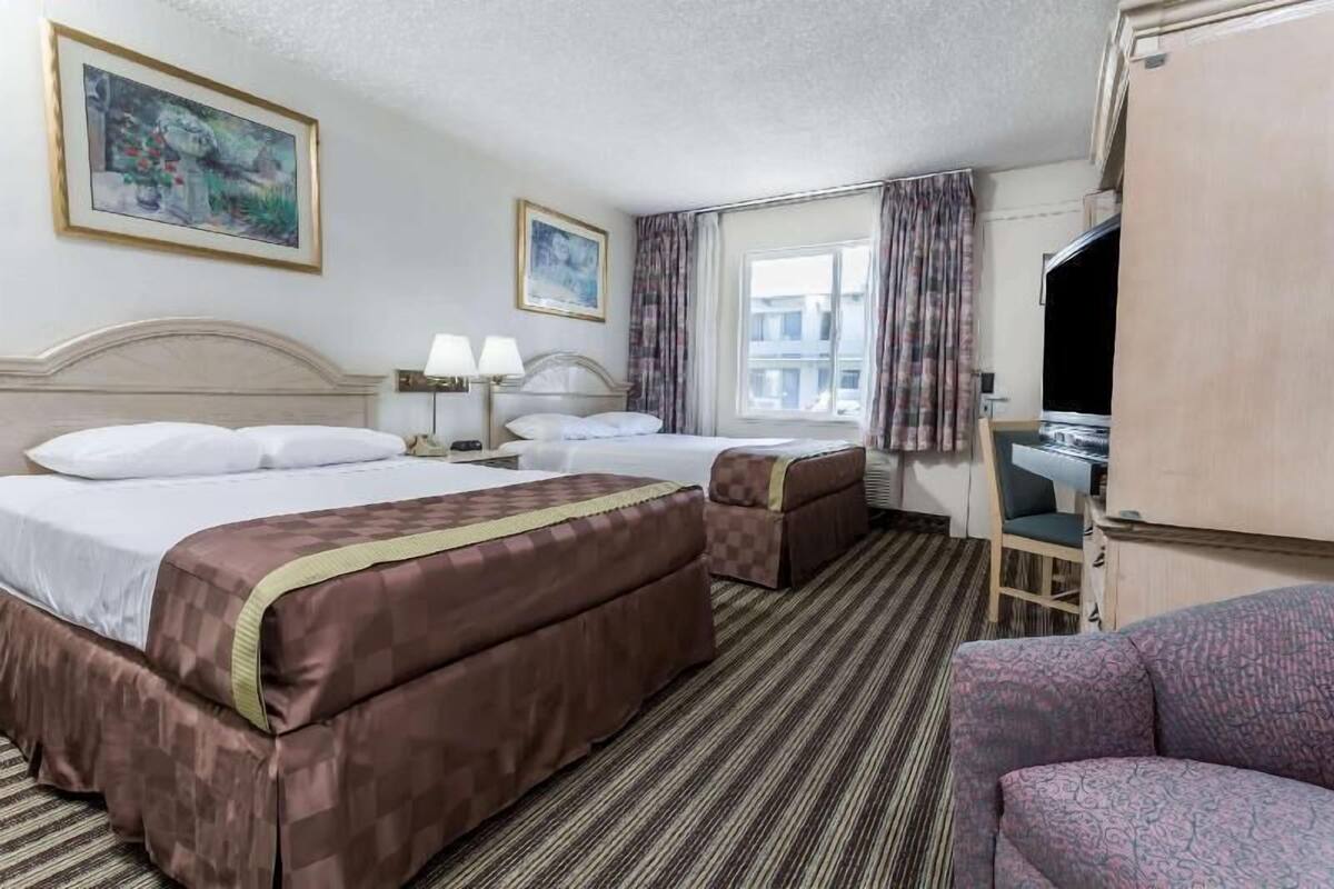A hotel room with two beds, a sofa, a desk, and a television.
