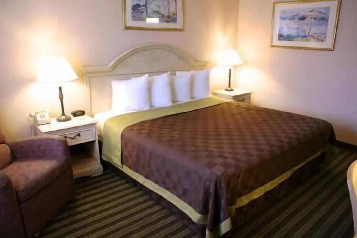 A hotel room with a bed, two bedside lamps, a chair, and a nightstand with a phone.