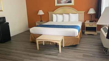 Hotelkamer met een groot bed, twee nachtkastjes, een klein nachtkastje, een bureau, een stoel, een verwarming en een foto aan de muur.