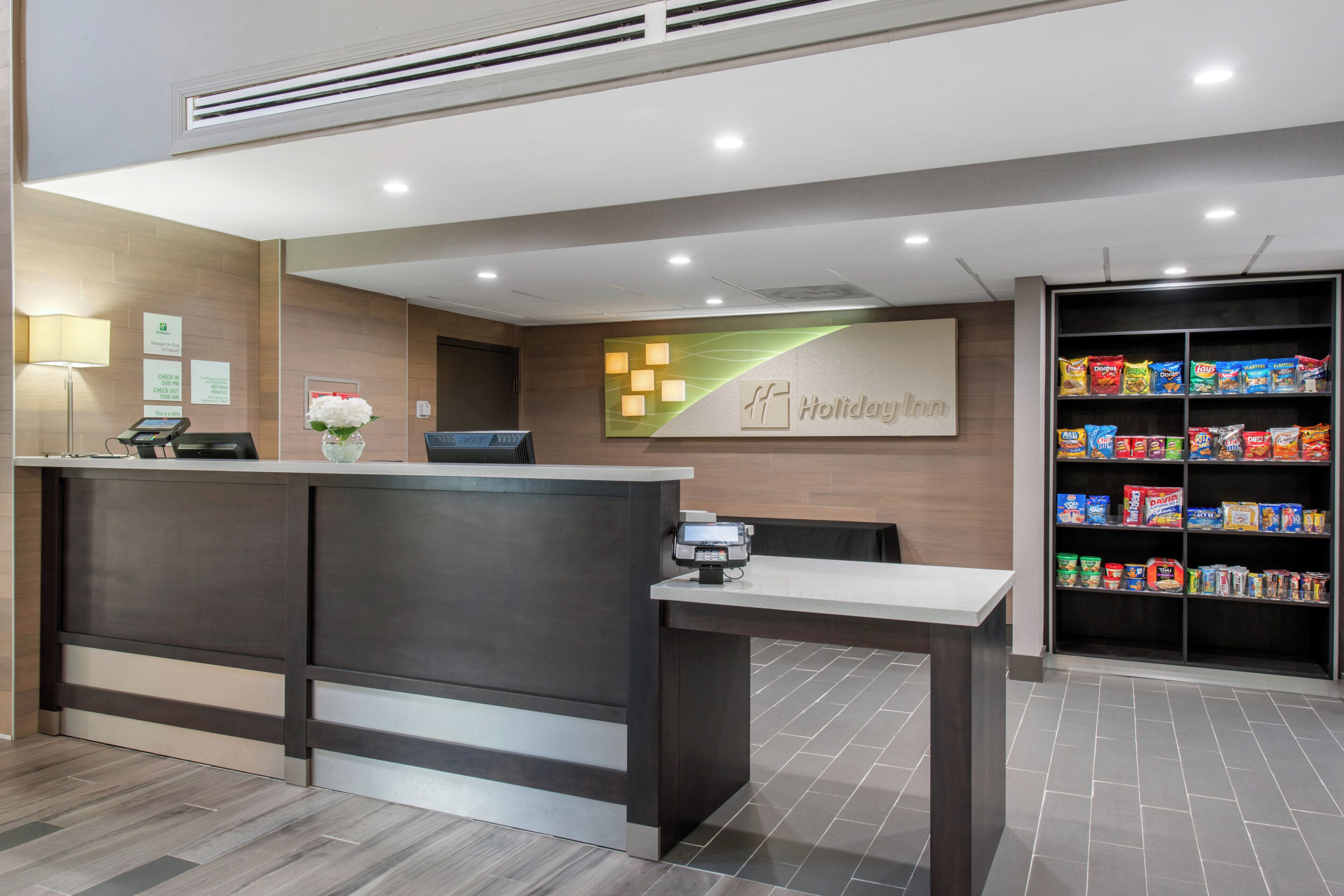 Un comptoir d’accueil d’hôtel doté d’un terminal d’enregistrement numérique, d’un vase de fleurs et d’une enseigne Holiday Inn.