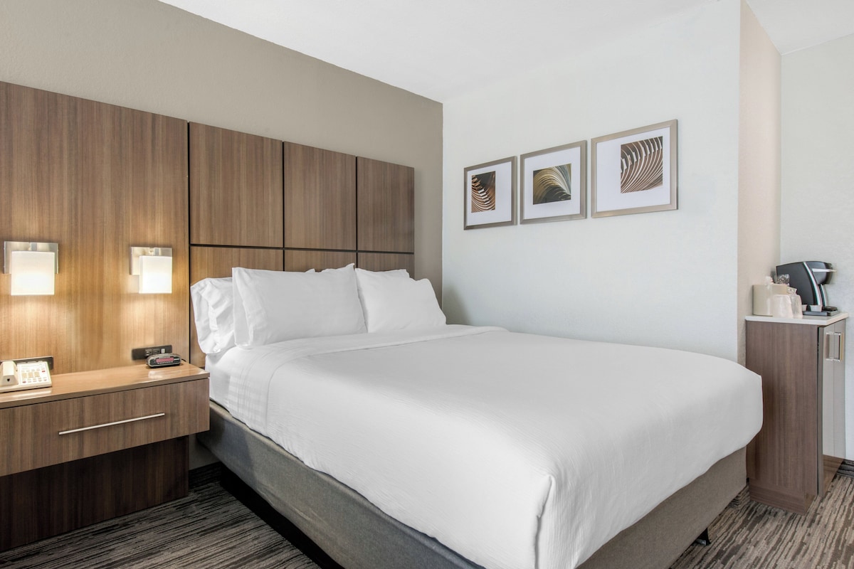 A hotel room with a large bed, a wooden headboard, a bedside table with a phone, and a wall-mounted light.