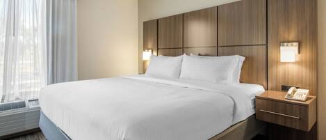 Una habitación de hotel con una cama grande, una mesita de noche con teléfono y una ventana con cortinas.