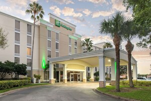 Un hotel Holiday Inn con entrada cubierta, palmeras y cielo despejado.