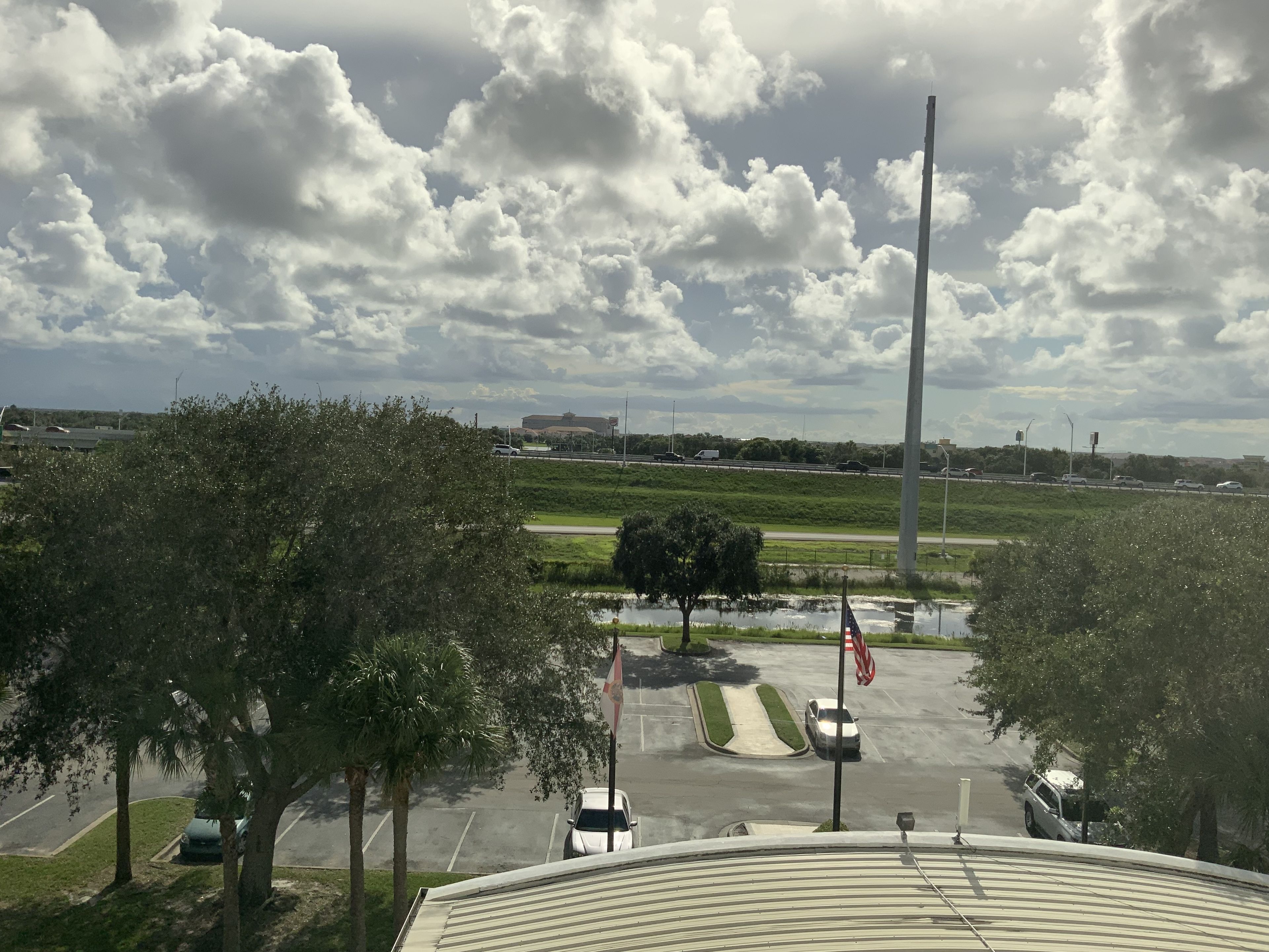 A parking lot with a flagpole, a flag, and a distant view of a highway and buildings.