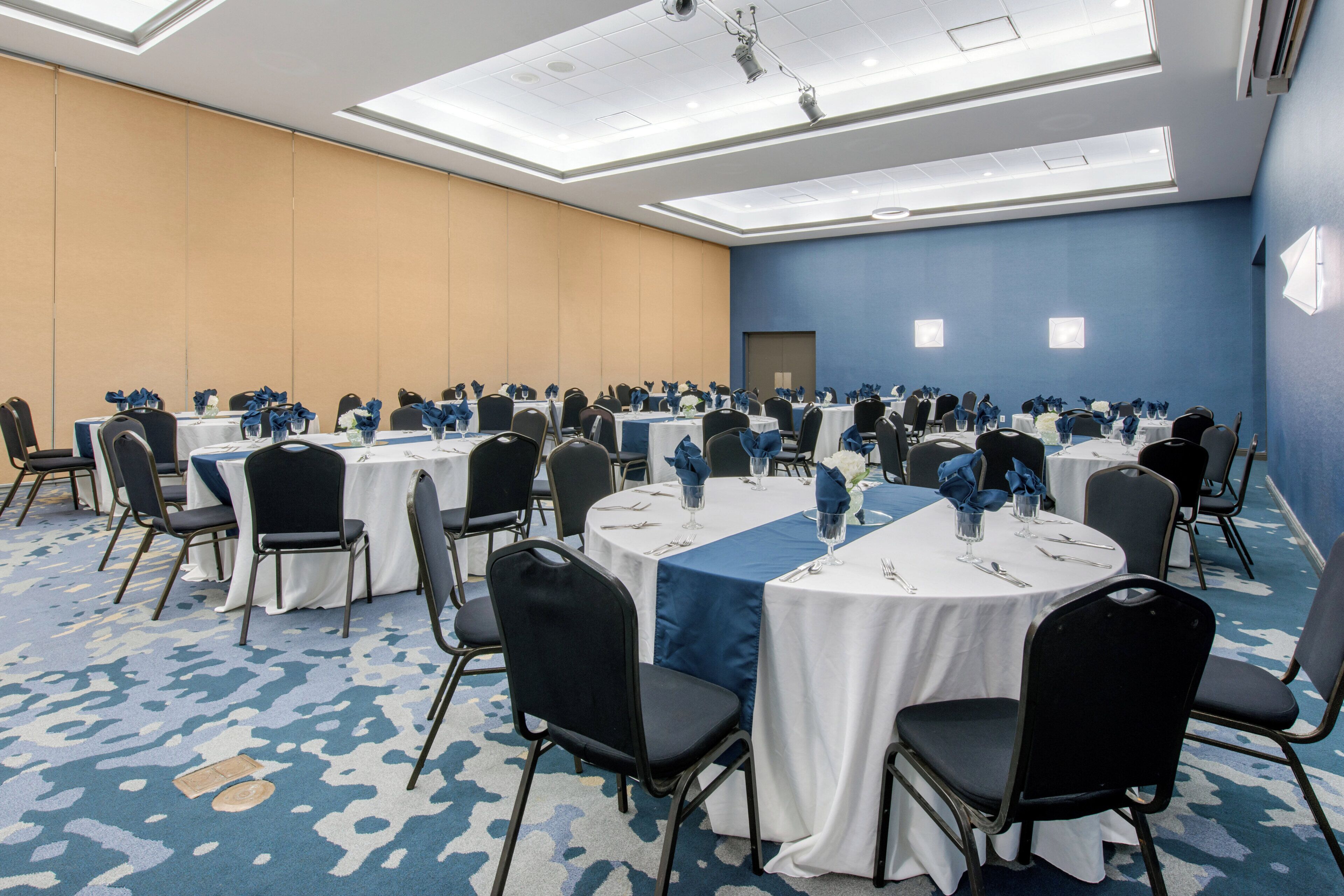 Un salón de conferencias con mesas redondas, sillas y alfombra azul.