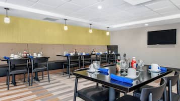 Une salle à manger d’hôtel avec plusieurs tables, des chaises et un téléviseur à écran plat fixé au mur.