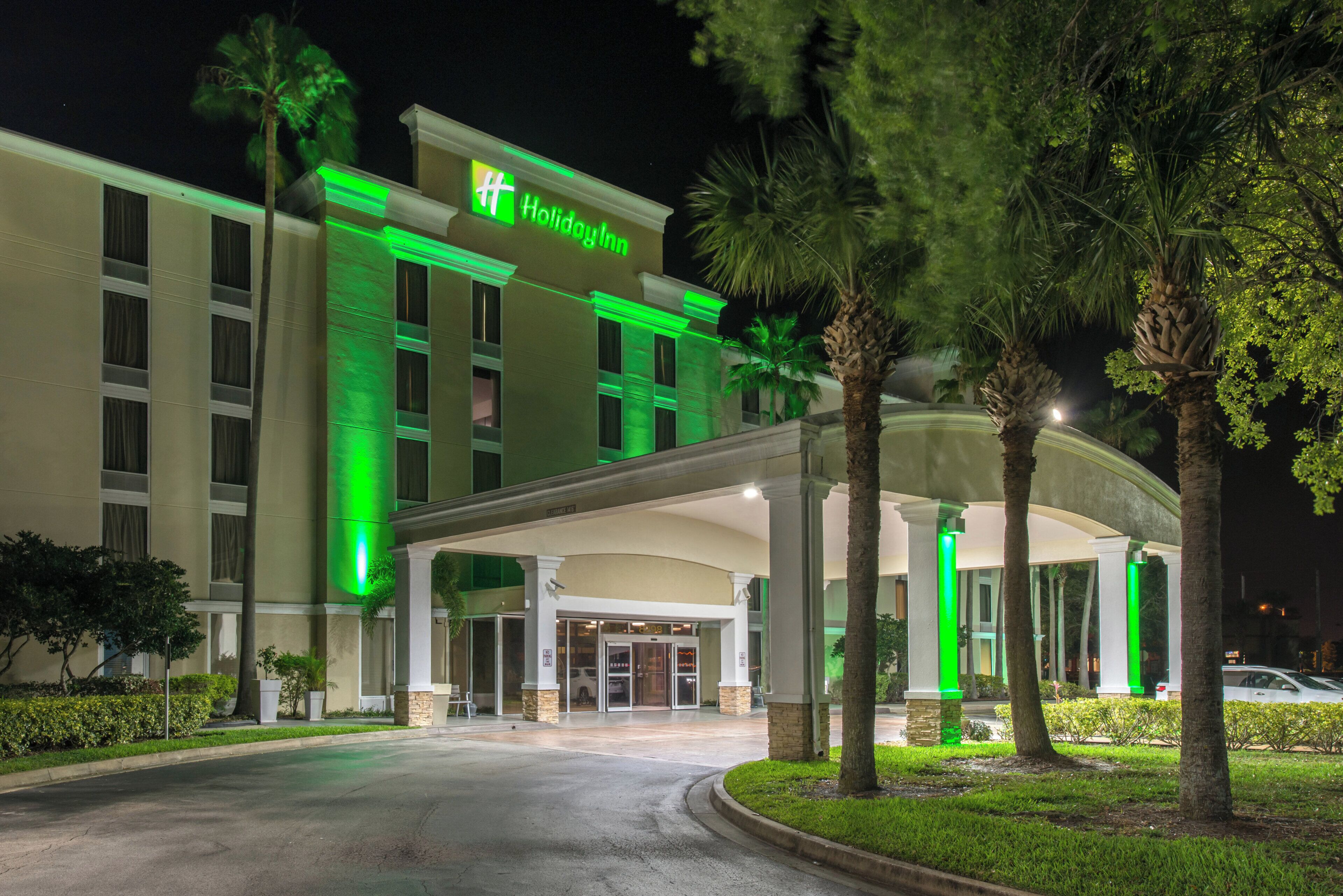 A Holiday Inn hotel with a covered entrance, palm trees, and a well-lit facade.