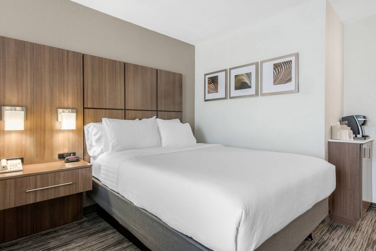 A hotel room with a large bed, a wooden headboard, bedside lamps, a nightstand, and a small cabinet.