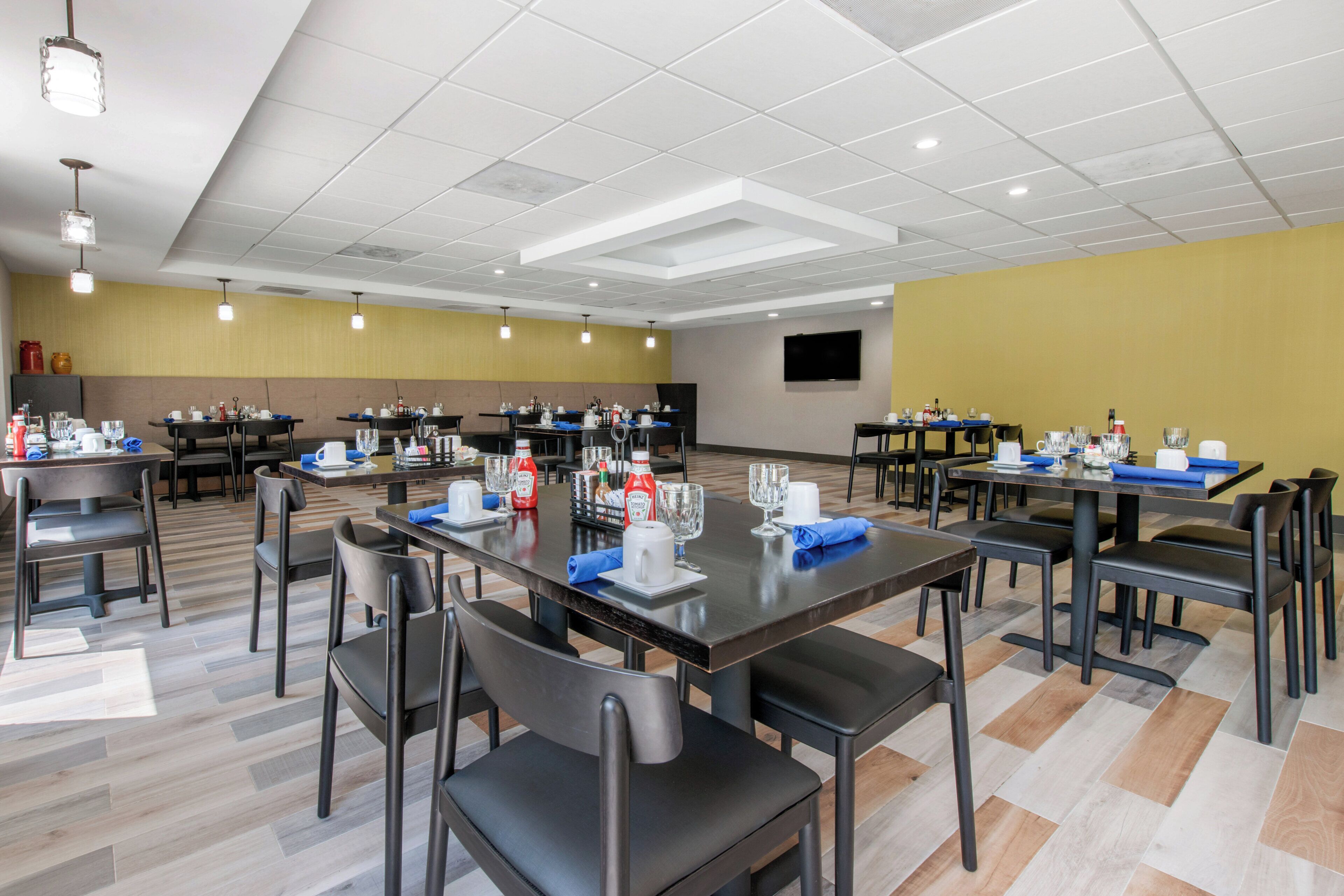 A conference room with multiple tables, chairs, and a flat-screen TV on the wall.