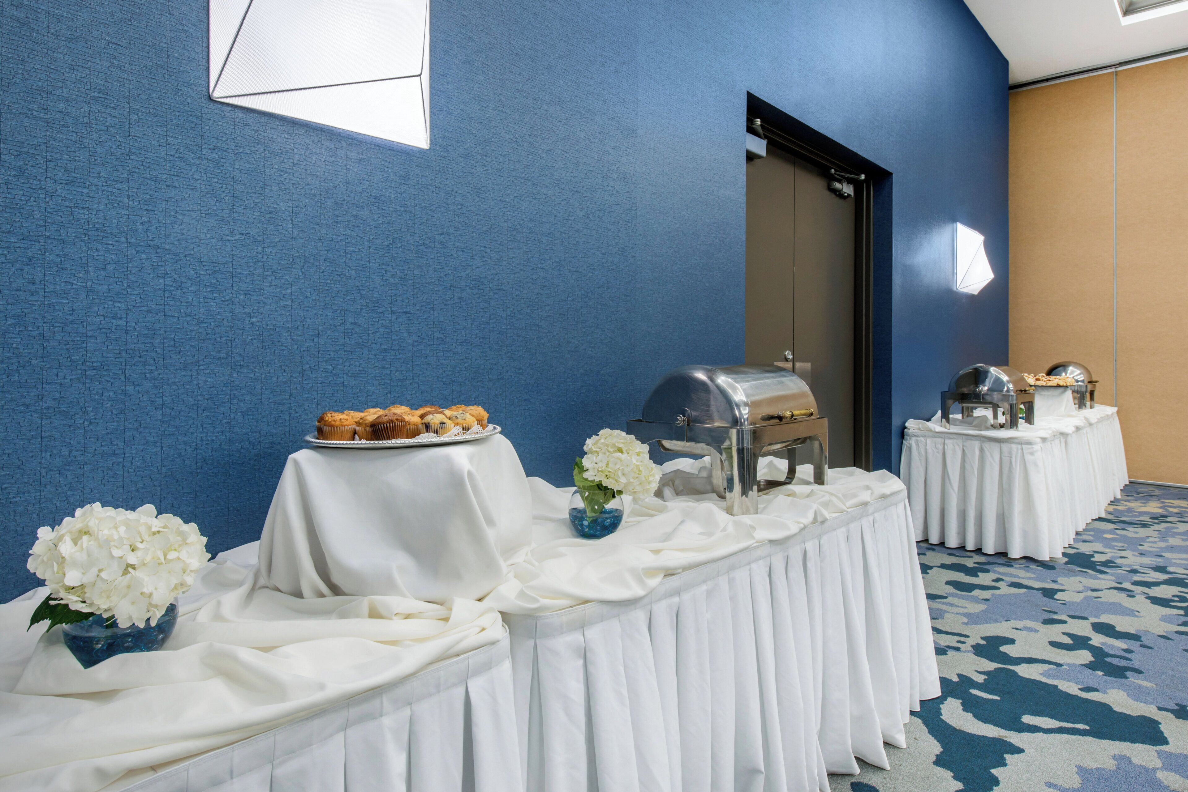 A room with a buffet table set up with food, a grill, and a decorative vase with flowers.