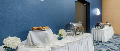 A room with a buffet table set up with food, a grill, and a decorative vase with flowers.