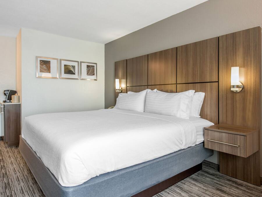 A hotel room with a large bed, wooden headboard, wall-mounted light fixtures, and framed artwork on the wall.