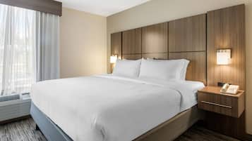 Une chambre d’hôtel avec un grand lit, une tête de lit en bois, des lampes de chevet, une table de chevet avec un téléphone et une fenêtre ornée de rideaux légers.