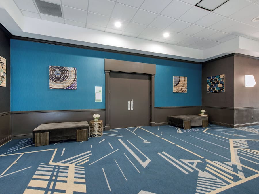 A hotel lobby with a blue carpet, artwork on the walls, a bench, and a door labeled 'EGRET ROOM'.