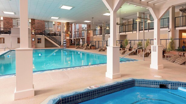 An indoor swimming pool with multiple levels, a clock, and lounge areas with chairs. - Delta Hotels by Marriott Kalamazoo Conference Center (Kalamazoo)