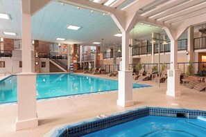 An indoor swimming pool with multiple levels, a clock, and lounge areas with chairs.
