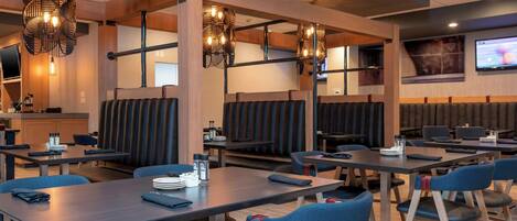 A restaurant with booths and tables, modern lighting, and a TV screen on the wall.