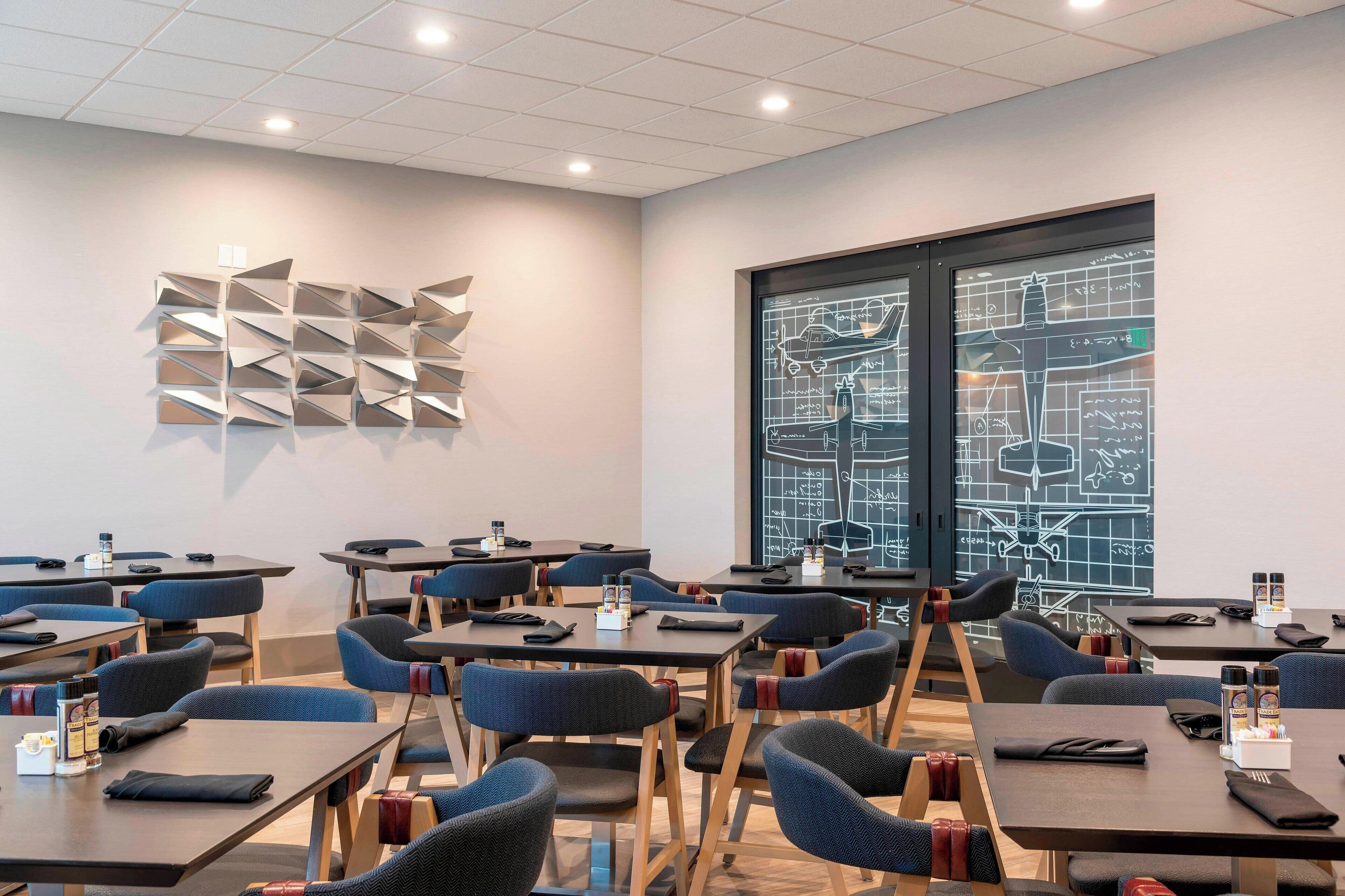 A conference room with tables, chairs, and a projector screen displaying a blueprint.