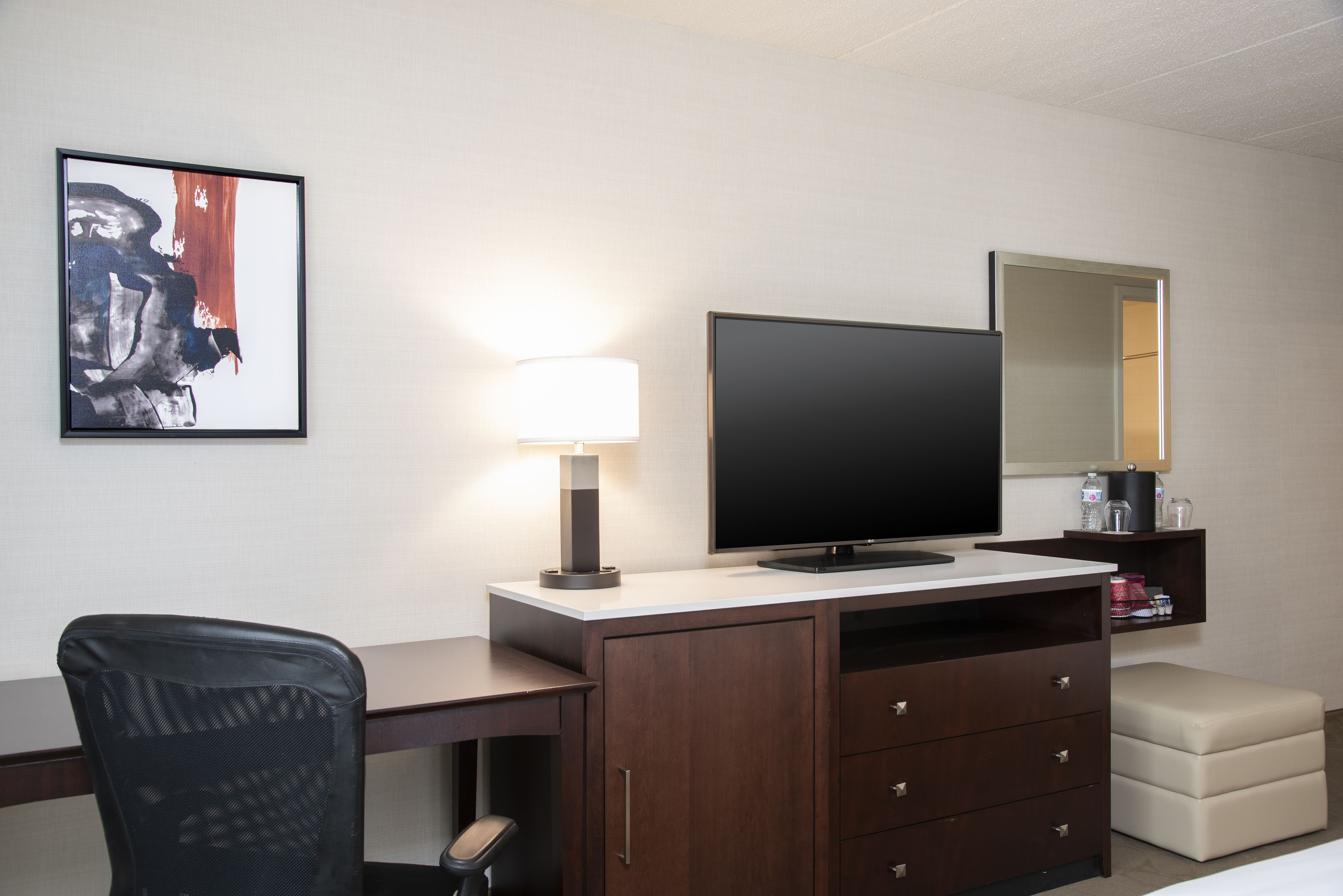 Une chambre d’hôtel équipée d’un bureau, d’une télévision, d’une lampe, d’une chaise, d’un canapé et d’une œuvre d’art encadrée accrochée au mur.