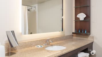 A bathroom with a granite countertop sink, a large mirror, a shower curtain, and a shelf with toiletries.