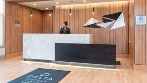 A hotel reception desk with a modern design, featuring a wooden panel wall and a geometric logo. - Delta Hotels by Marriott Kalamazoo Conference Center (Kalamazoo)