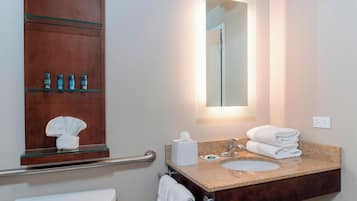 Un bagno con uno scaffale in vetro contenente articoli da toilette, un lavandino con una pila di asciugamani e uno specchio sopra il lavandino.