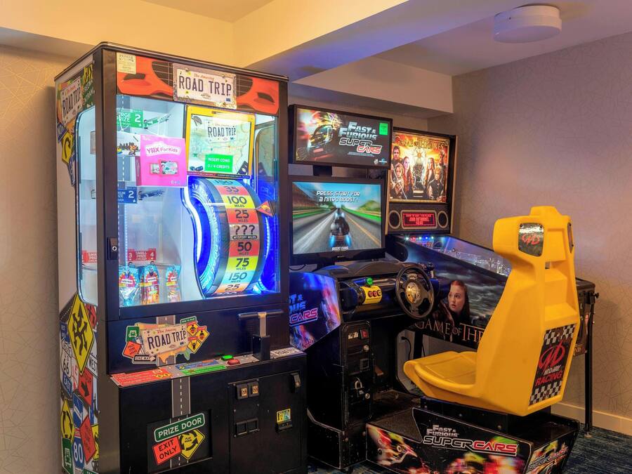Una sala de juegos de carreras con varias pantallas y un asiento de carreras amarillo.