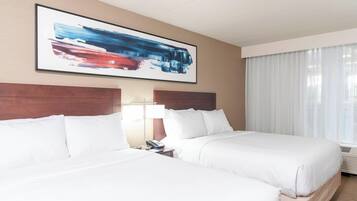 A hotel room with two beds, a large abstract painting on the wall, a bedside lamp, and a window with curtains.